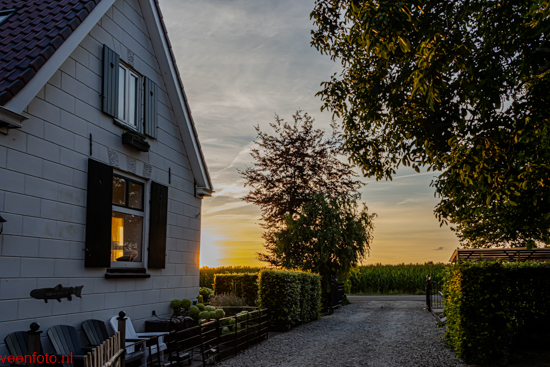 Zonsondergang boven het erf, met de witte gevel en terrasstoelen