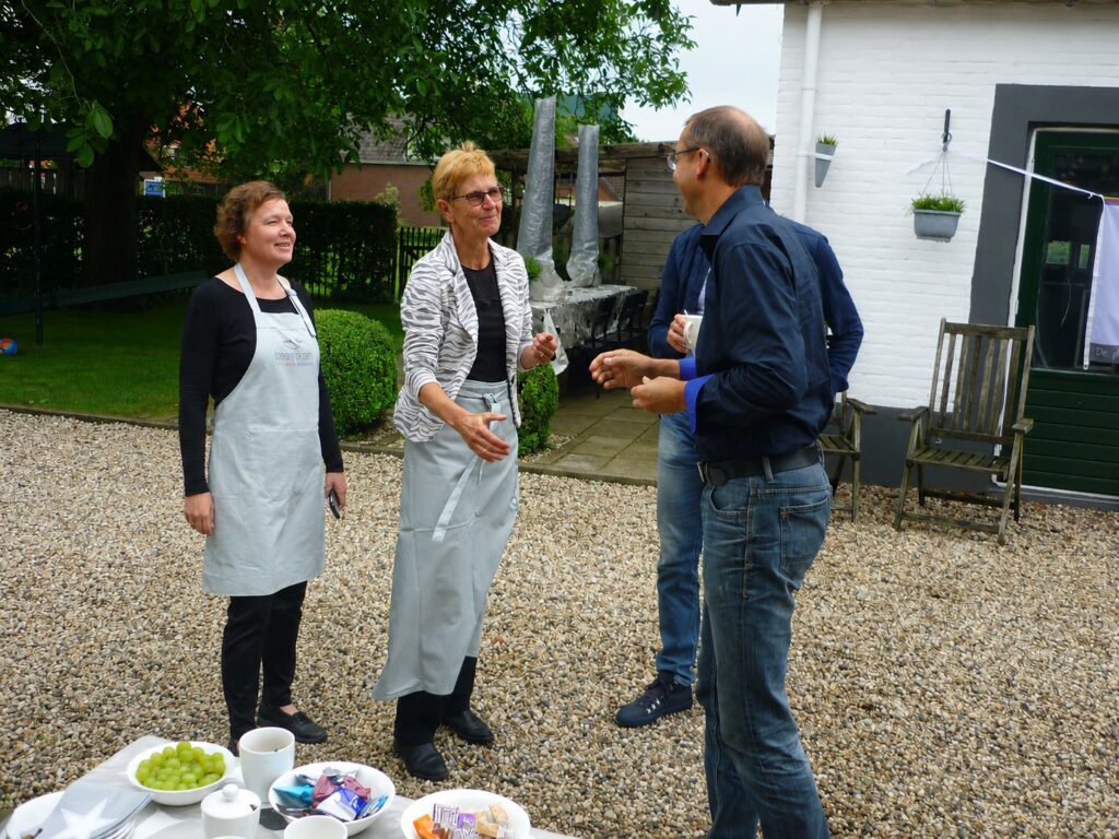 Astrid in gesprek met gasten op het erf bij een gedekte tafel