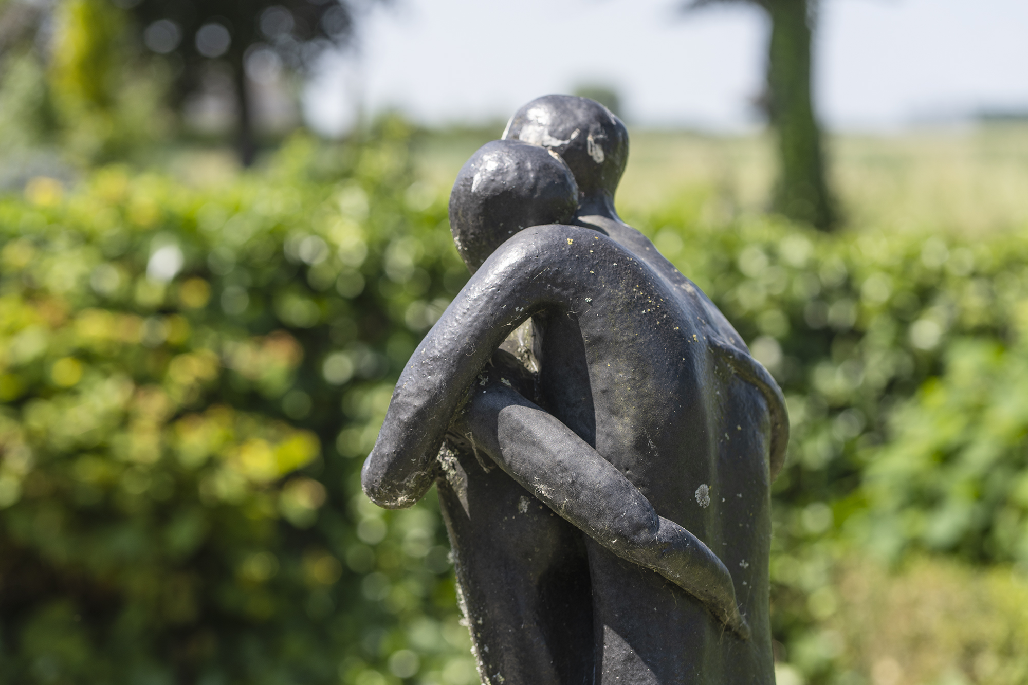 Bronzen beeld van een zittende figuur tussen het groen