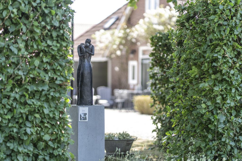 Beeld van een vrouw voor de boerderij, tussen de hagen