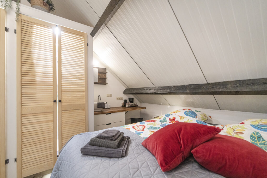 Bed met rode kussens en handdoeken in een loft onder een schuin dak