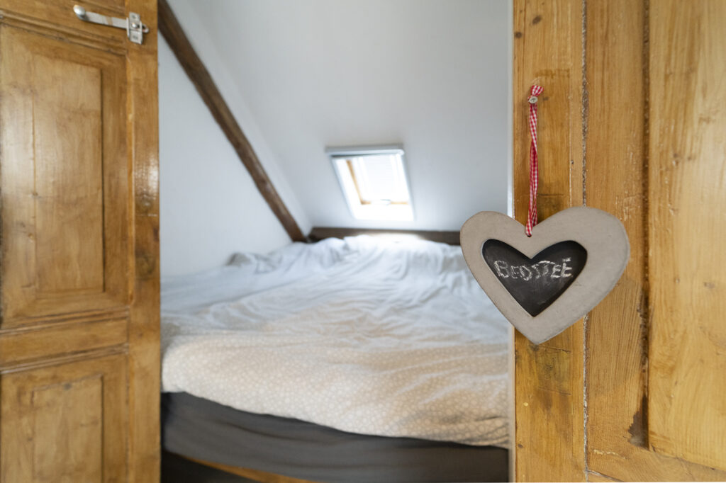 Tweepersoonsbed onder een schuin dak met een houten hartje aan de deur