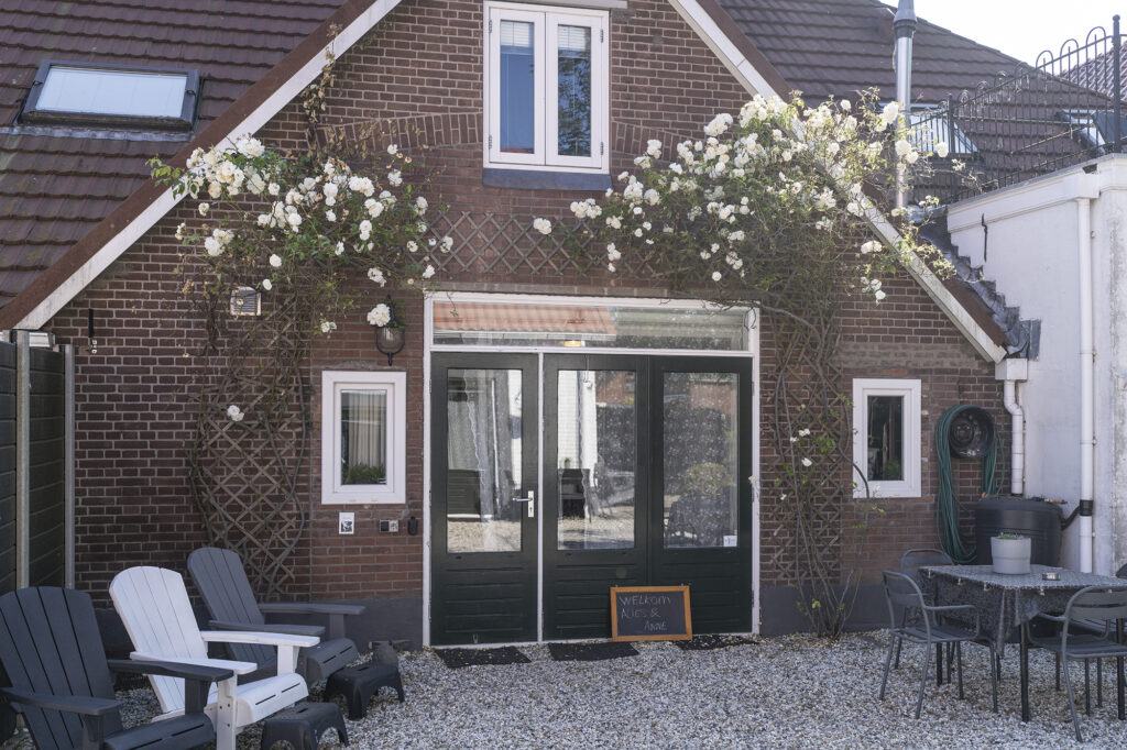 Bakstenen gevel met rozen rond de voordeur en loungestoelen op het terras
