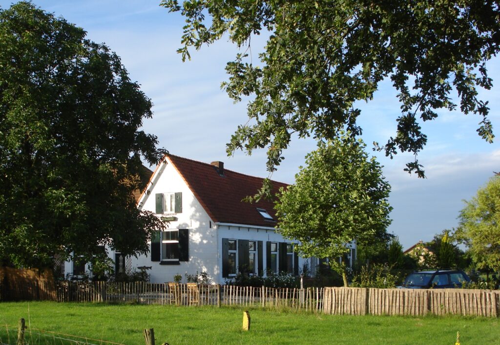 Witte boerderij achter een houten hek tussen hoge bomen, Boerderij de Zalm in Schalkwijk